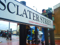Street name board for Sclater Street. In the background is a road and people on the pavement.