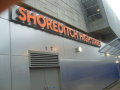 A shot of the Shoreditch High Street overground station board on the metal wall.