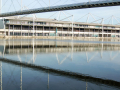 On foot, the view of the back of ExCeL with the bridge above casting its shadow on the river.