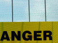 The word ANGER on a yellow sign, hanging from a grey fence