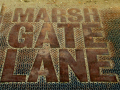 A large, rusted plaque on the ground with the words MARSH GATE LANE on it