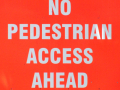 The words NO PEDESTRIAN ACCESS AHEAD in white, against a vibrant red background